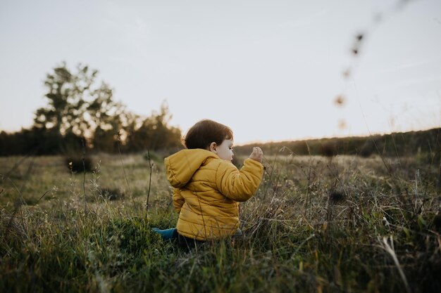 Foto vista trasera de un niño sentado en la hierba contra el cielo