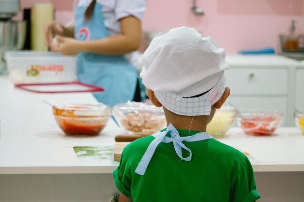 Foto vista trasera de un niño con sombrero de chef cocinando comida en la cocina