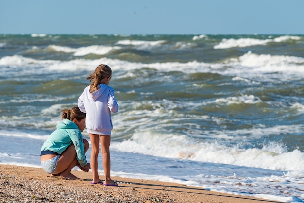 Vista trasera de niños pequeños jugando en la playa en la arena cerca de las olas del mar tempestuoso