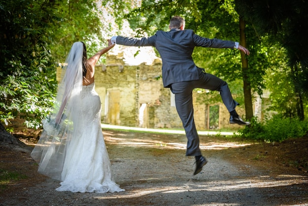 Vista trasera del novio saltando mientras sostiene la mano de la novia en el sendero