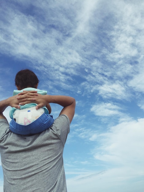 Foto vista trasera del padre llevando al bebé en los hombros contra el cielo