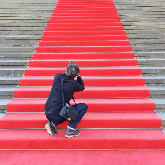 Foto vista trasera de un paparazzi masculino en las escaleras con alfombra roja