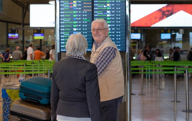 Vista trasera de una pareja de ancianos de pelo blanco empujando un carrito de equipaje caminando en la zona del aeropuerto