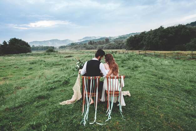 Foto vista trasera de la pareja de bodas sentada en sillas en una granja
