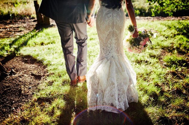 Vista trasera de la pareja de bodas tomados de la mano mientras caminan por el campo