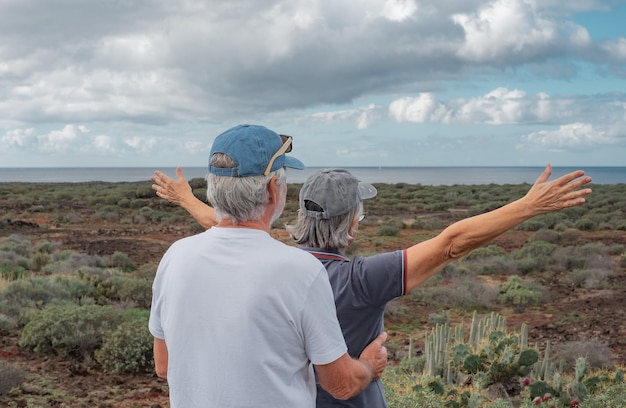 Vista trasera de la pareja caucásica mayor en el camino del campo mirando el mar sintiéndose libre