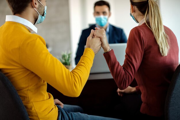 Vista trasera de una pareja cogida de la mano durante una reunión con un agente inmobiliario en la oficina