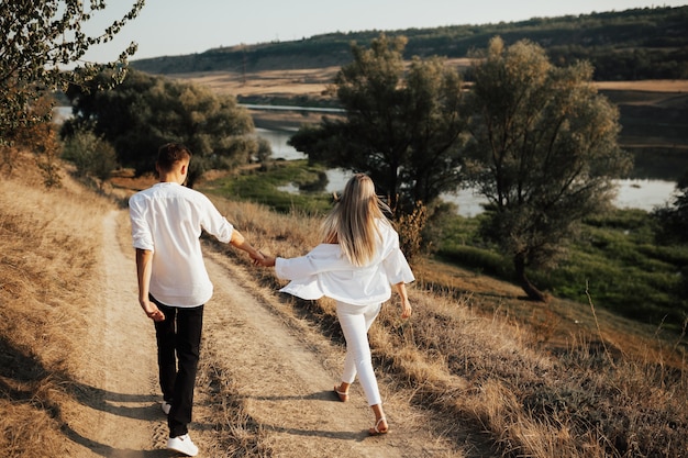 Vista trasera de la pareja cogidos de la mano y caminando en un hermoso campo. Pareja joven caminando por la carretera.