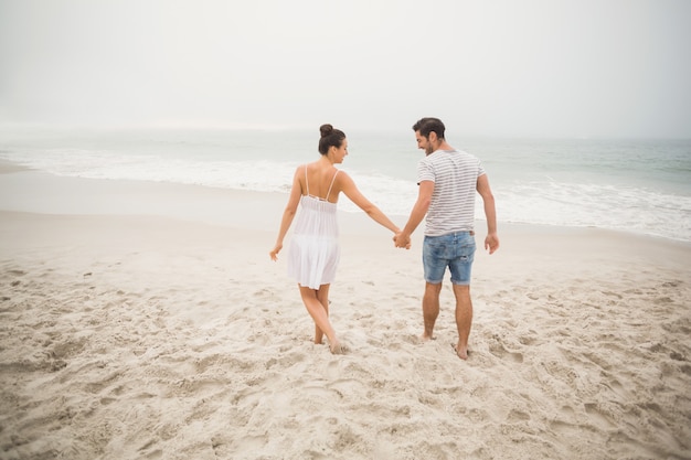 Vista trasera de la pareja cogidos de la mano y caminando por la playa