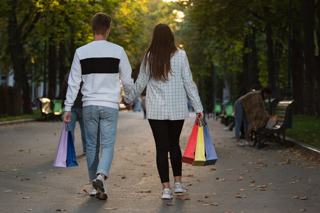 Vista trasera de la pareja de enamorados caminando en el parque con bolsas de la compra.