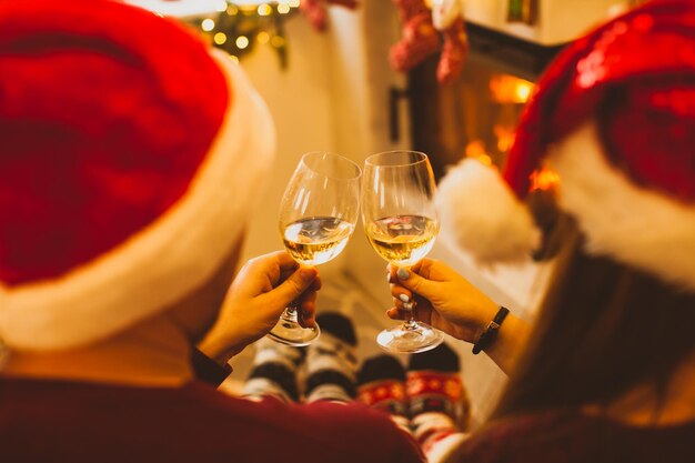 Vista trasera de una pareja joven con sombreros de Santa sosteniendo copas de champán o vino blanco brindando Hombre y mujer en calcetines calientes cerca de la chimenea