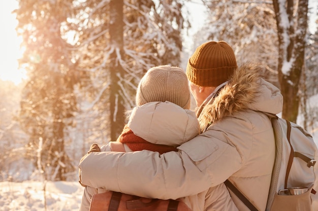 Vista trasera de una pareja madura abrazándose en un bosque invernal iluminado por el espacio de la luz del sol