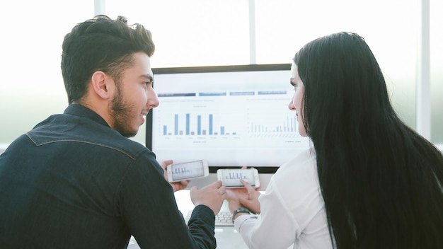 Vista trasera.Pareja de negocios discutiendo gráficos financieros, sentado en su escritorio.La gente y la tecnología