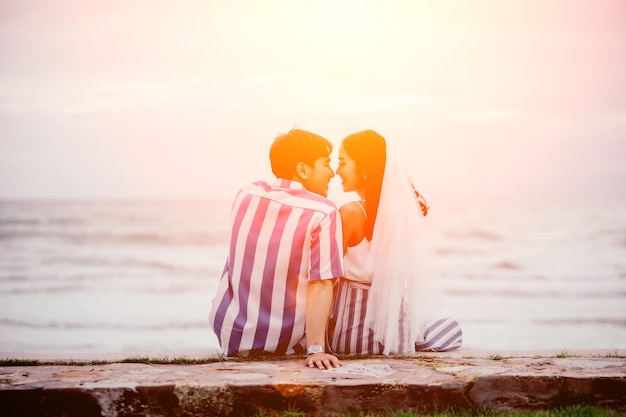 Foto vista trasera de una pareja sentada en una pared de contención contra el mar durante la puesta de sol