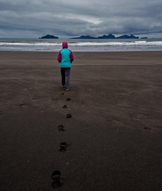 Foto vista trasera de una persona caminando en la playa contra un cielo nublado