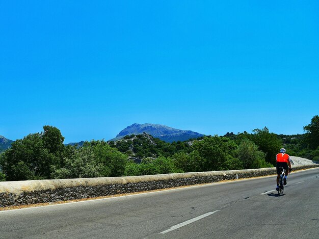 Foto vista trasera de una persona montando una bicicleta en la calle contra un cielo azul claro