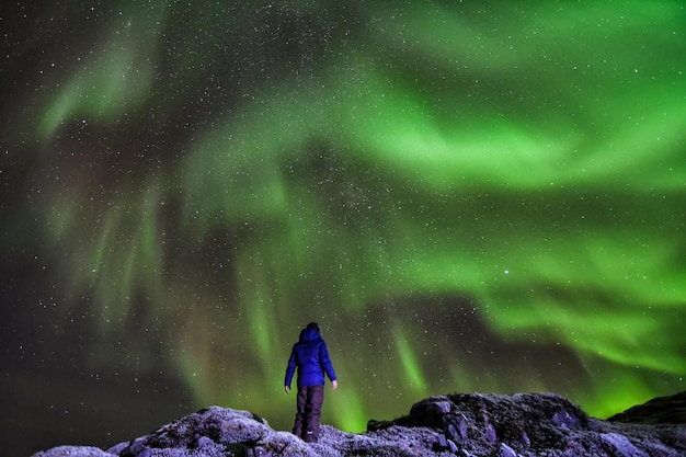 Vista trasera de una persona de pie en una roca contra las luces del norte por la noche
