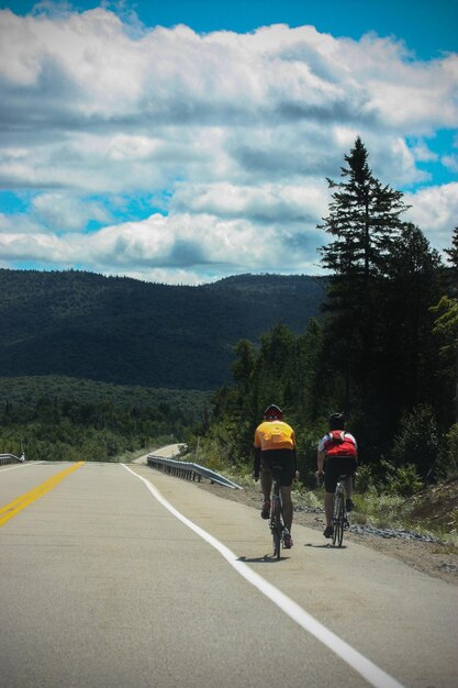 Foto vista trasera de personas en bicicleta en la carretera contra el cielo