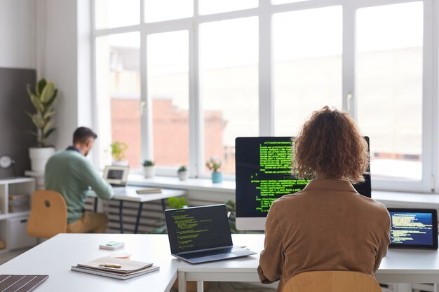 Vista trasera de personas que trabajan con nuevo software en computadoras en la mesa de la oficina