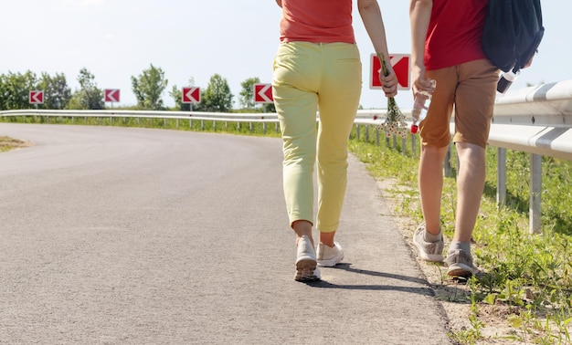 Vista trasera de las piernas de una mujer delgada y un hombre caminando juntos por la carretera Concepto de viaje y senderismo