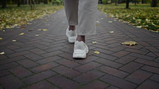 Vista trasera de los pies del hombre caminando a lo largo del parque de otoño durante el día La cámara sigue a las piernas del hombre desconocido pasando el tiempo libre en el lugar de follaje Los pies masculinos irreconocibles en el parque de octubre