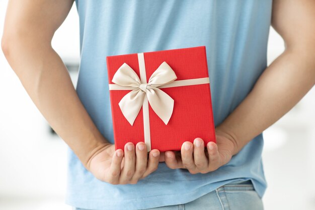 Foto vista trasera de primer plano del hombre en camiseta azul con caja de regalo detrás de su espalda mientras