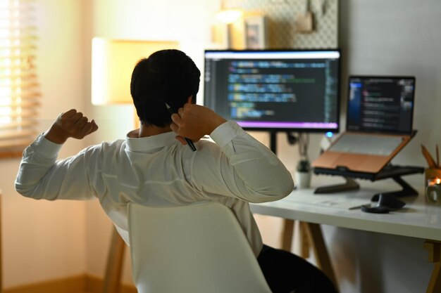 Vista trasera de un programador masculino estirando los brazos y relajándose en una silla en su lugar de trabajo