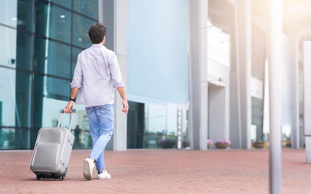 Vista trasera retrato de hombre caminando fuera del aeropuerto con maleta