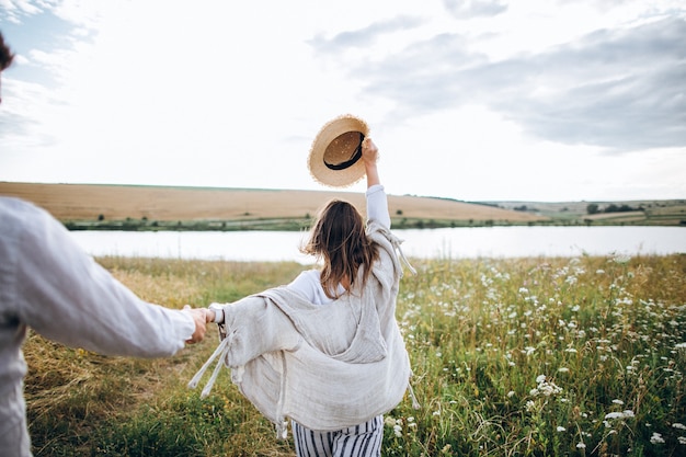 Vista trasera sígueme. Feliz pareja de enamorados abrazándose, besándose y sonriendo contra el cielo en el campo.