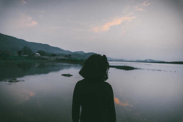 Foto vista trasera de la silueta de una mujer de pie junto al lago