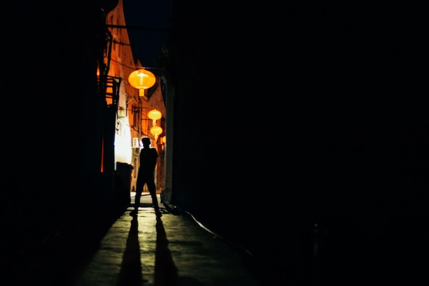 Vista trasera de una silueta de niño caminando por una calle iluminada por la noche