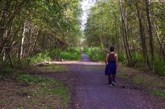 Foto vista trasera a toda longitud del hombre caminando entre los árboles en el bosque