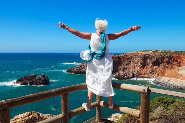 Vista trasera de toda la longitud de la mujer con los brazos extendidos sobre la barandilla contra el mar