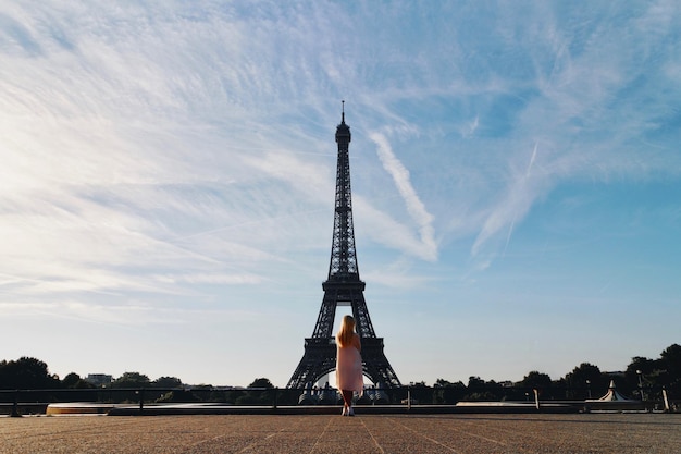 Vista trasera a toda longitud de una mujer de pie contra la Torre Eiffel