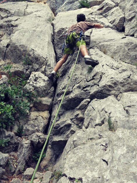 Foto vista trasera en toda su longitud de un escalador que sube a la roca