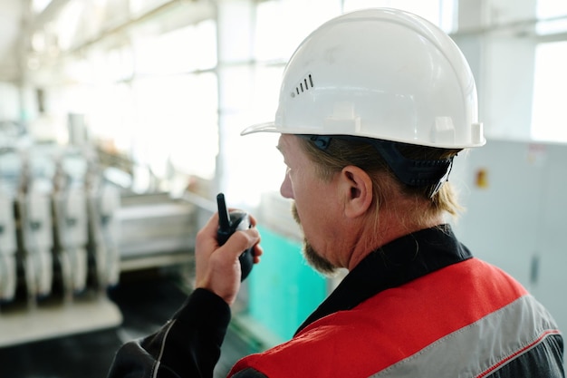 Vista trasera del trabajador con casco usando un aparato de radio en su trabajo en la planta