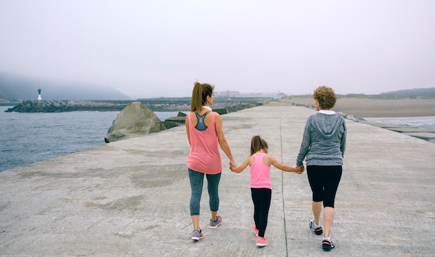 Vista trasera de tres generaciones femeninas caminando por el muelle del mar