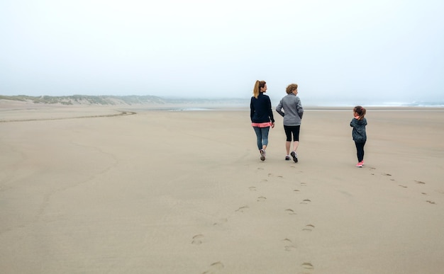 Vista trasera de tres generaciones de mujeres caminando por la playa en otoño