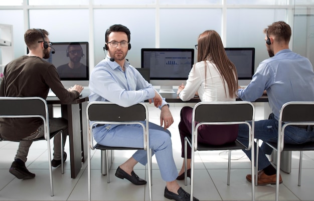 Foto vista traserahombre de negocios con auriculares y sus colegas sentados en la oficina