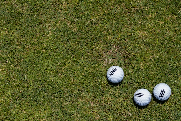 Vista de tres pelotas de golf en una esquina en un fondo de la hierba verde.