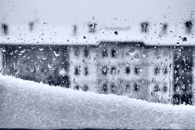 Vista desde la ventana al deshielo invernal Ventisquero derretido y gotas sobre el vidrio Edificio de varios pisos con muchas ventanas Postal navideña de Año Nuevo Melancolía y lágrimas o la llegada de la primavera