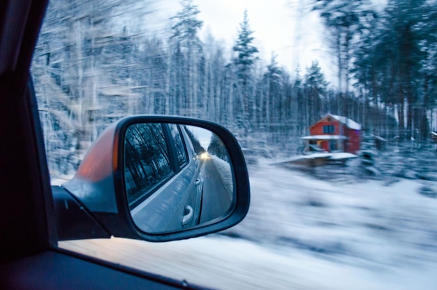 La vista desde la ventana del auto, el espejo retrovisor y el bosque cubierto de nieve.