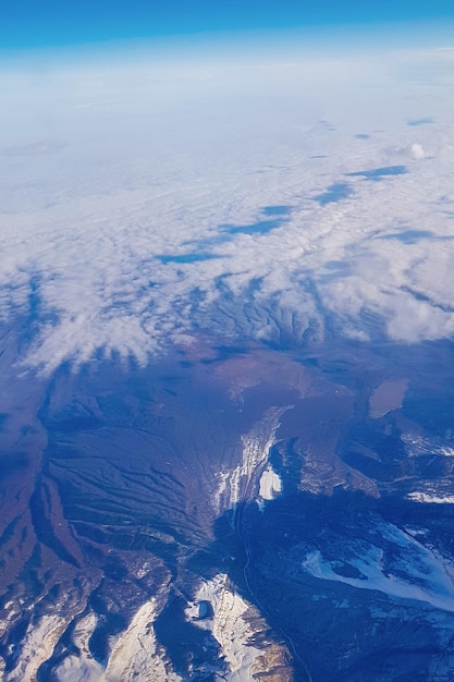 Vista desde la ventana del avión al cielo azul y picos montañosos nevados en nubes blancas