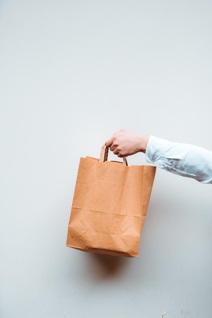 Vista vertical de la desconocida mujer milenaria sosteniendo una bolsa de papel con comida para llevar en el fondo blanco