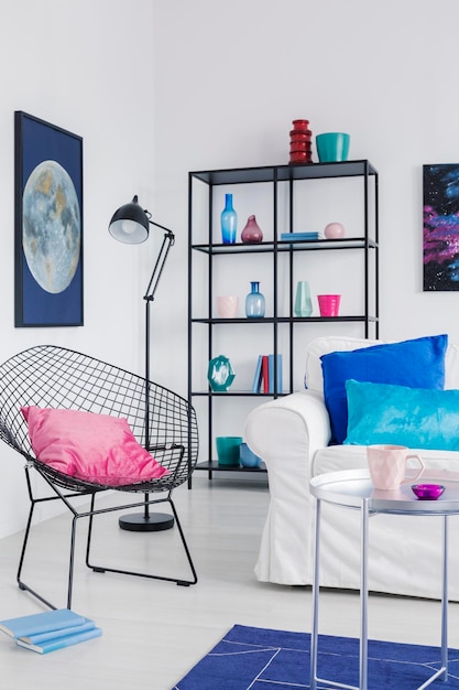 Vista vertical del elegante sillón con almohada rosa en el interior de la moderna sala de estar con sofá blanco y gráfico de luna en la pared