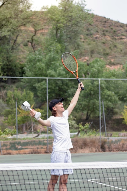 Vista vertical del joven atleta de tenis disfrutando de su victoria con expresión de cara feliz y emocionada Sosteniendo una taza