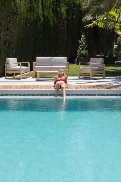 Vista vertical de una joven tendida en el borde de la piscina tomando el sol para broncearse en verano