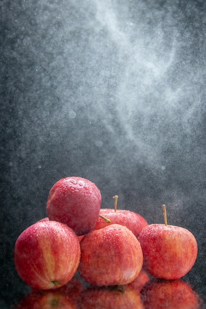 Vista vertical de manzanas rojas frescas apiladas en luz sobre fondo oscuro de la onda