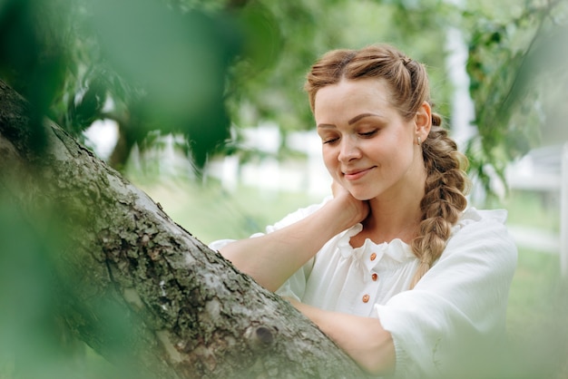 La vista vertical de la modelo femenina cerró los ojos y disfruta del aire fresco mientras está de pie en un campo con hierba verde. Hermosa mujer joven con cabello castaño. Concepto de naturaleza