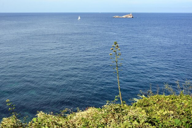 Vista de un yate lejano en el mar y una isla en el horizonte bajo un cielo azul